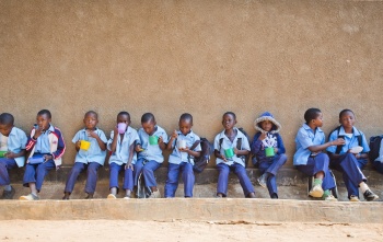 Djeca sjede uz zid u školi dok zajedno jedu.