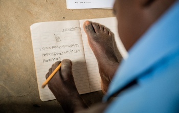 Djevojčica piše u bilježnicu držeći olovku lijevom nogom