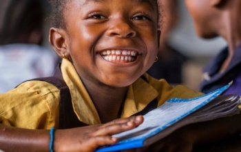 Djevojčica s knjigom na stolu se smješka kameri