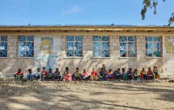 Dječaci sjede uza zid škole i uživaju u svom obroku