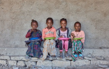 Četiri djevojčice sjede naslonjene na zid i jedu svoje obroke