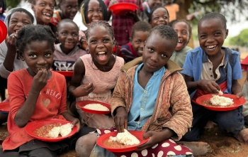 Djeca sjede na podu, jedu kašu i radosno poziraju za slikanje