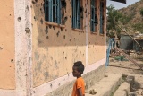 Dječak ispred škole čiji su zidovi puni rupa od metaka