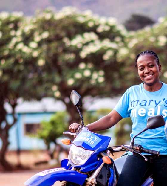 Službenica za prehranu u školi u Zambiji odmara se naslonjena na svoj motocikl.