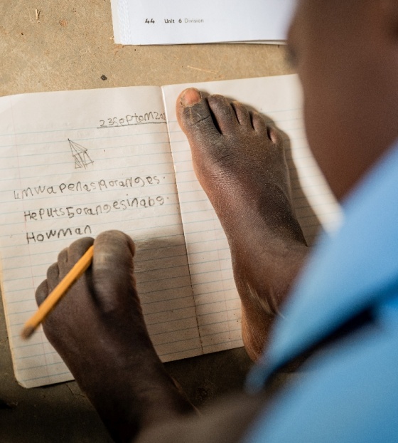 Djevojčica piše u bilježnicu držeći olovku lijevom nogom