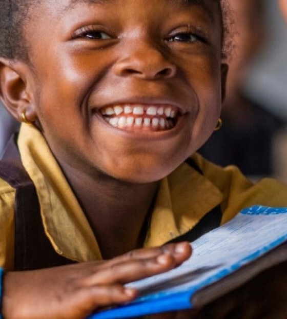 Djevojčica s knjigom na stolu se smješka kameri