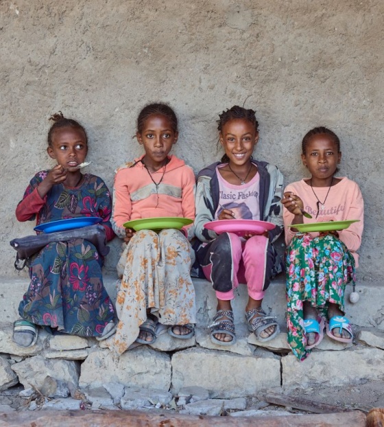 Četiri djevojčice sjede naslonjene na zid i jedu svoje obroke