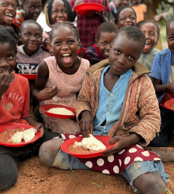 Djeca sjede na podu, jedu kašu i radosno poziraju za slikanje